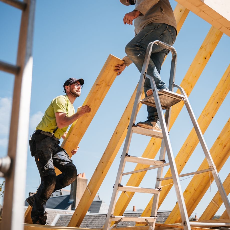 Illustrative licensed photograph: Two builders installing wooden roof framing