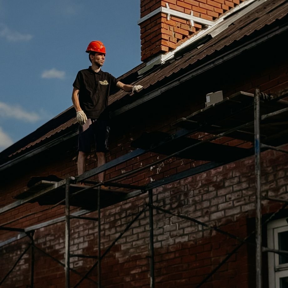 Illustrative licensed photograph: Roofer working on scaffold beside brick chimney