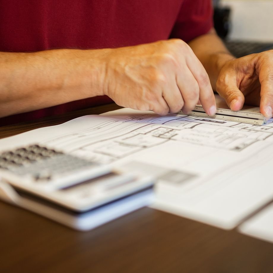 Illustrative licensed photograph: Hands measuring blueprints